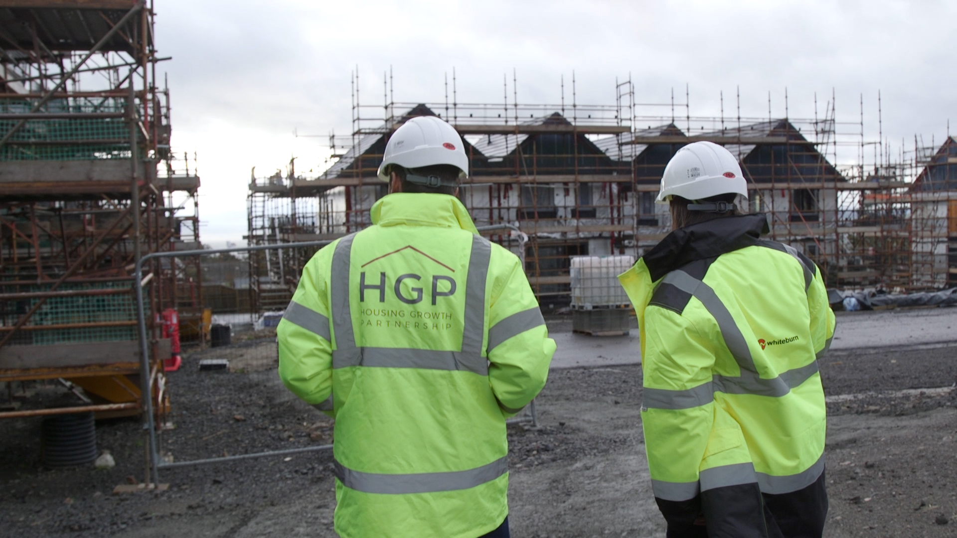Two Housing Growth Partnership employees in helmets and high visibility jackets looking at a housing development.