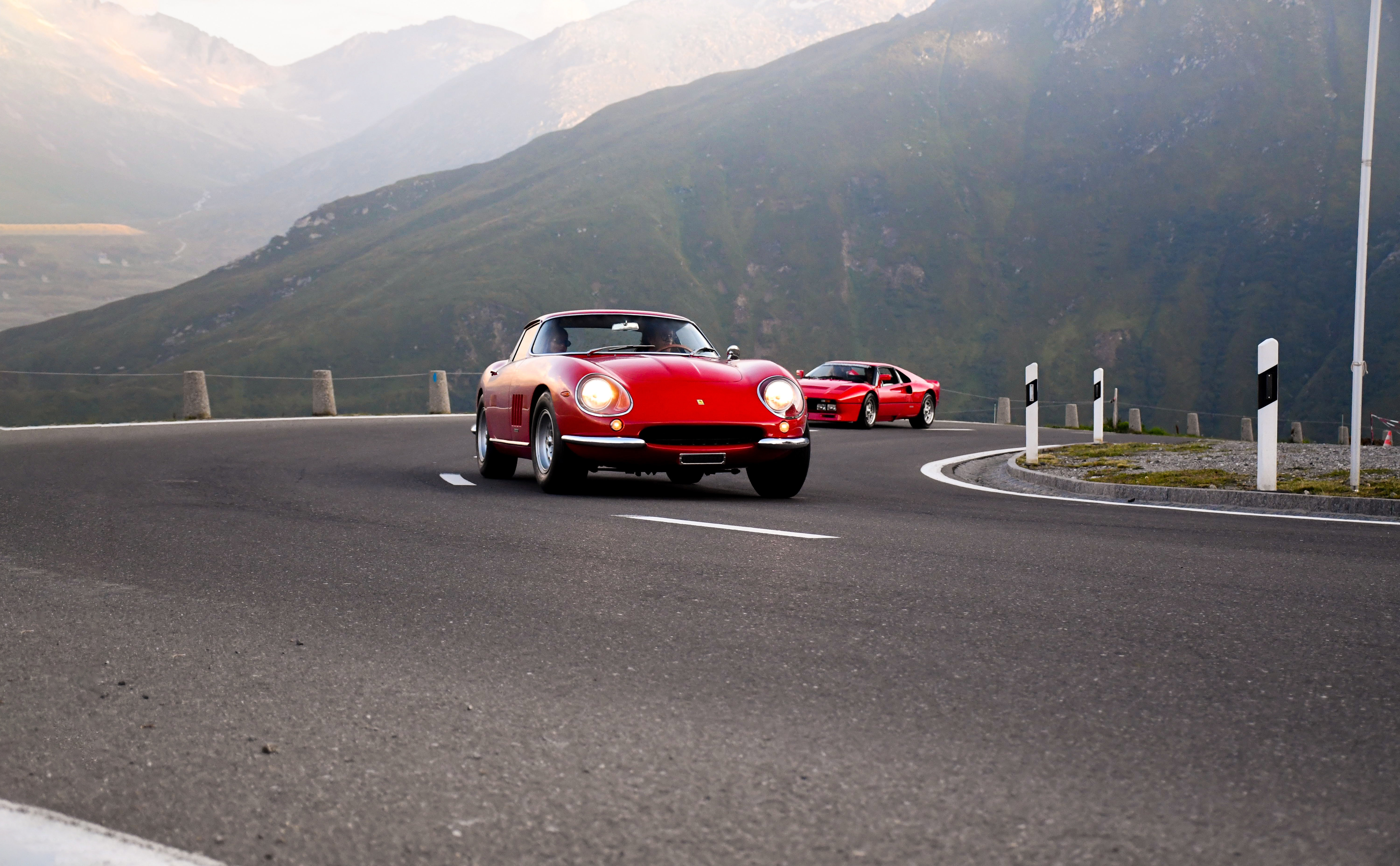 Two red cars driving up a mountain road.